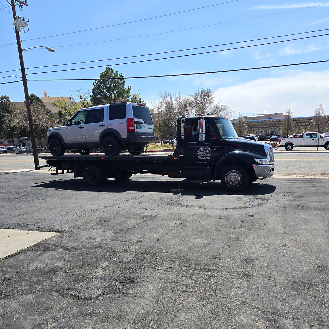 Flatbed tow truck transporting a silver SUV on a city street in New Mexico