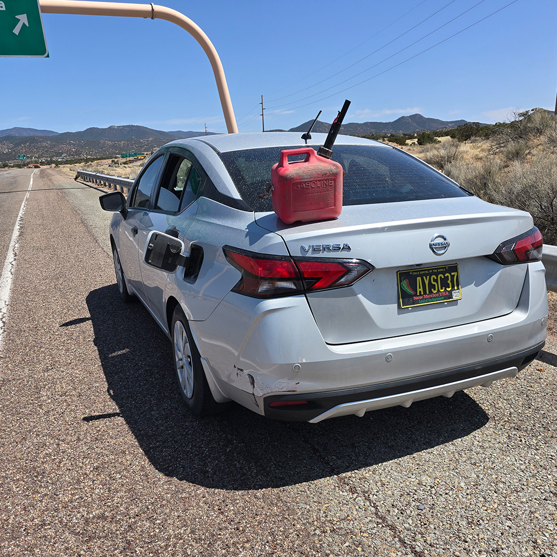 Stranded Nissan Versa with gas can on trunk near freeway exit in New Mexico
